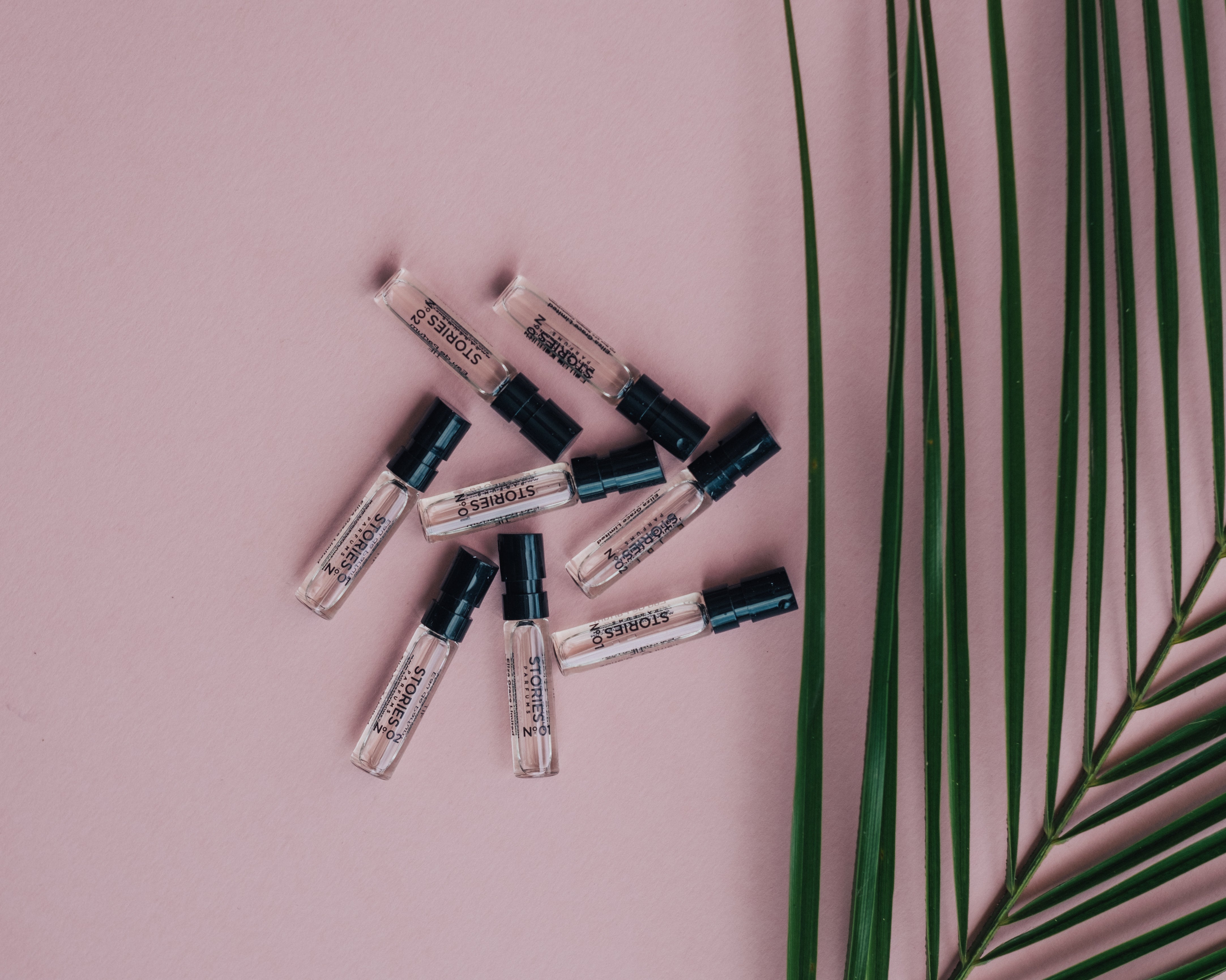 A pile of STORIES Parfums perfume samples on a pink background with green leaves