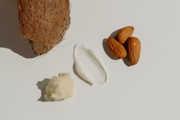 Hand squeezing lotion from black tube of STORIES hand and body lotion ingredients inc coconut shell and almonds on white background