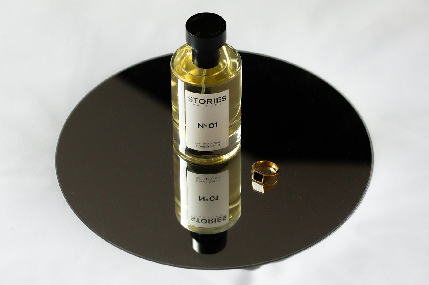 luxury perfume STORIES Parfums sat on reflective mirror surface with gold jewellary