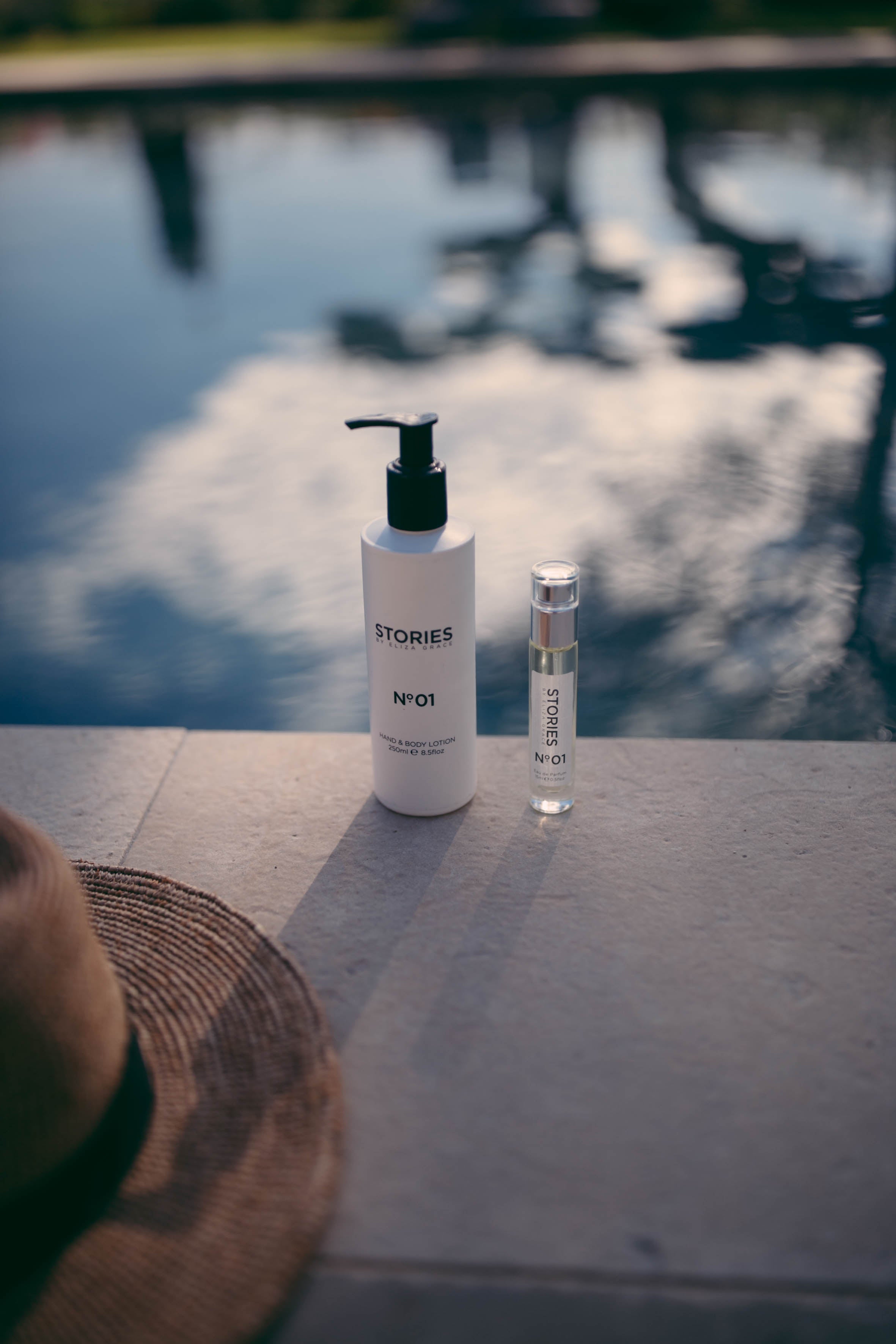 STORIES Parfums body wash and fragrance by a pool with reflections of clouds on the water