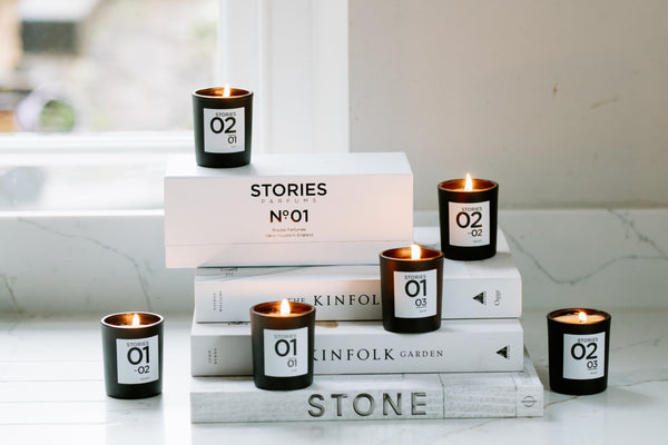 STORIES Parfums scented candles in black glass votives, lit and displayed on pile of white books and box