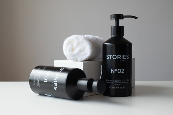 Two black bottles from STORIES body collection one upright and one on side next to a white box and white rolled up towel