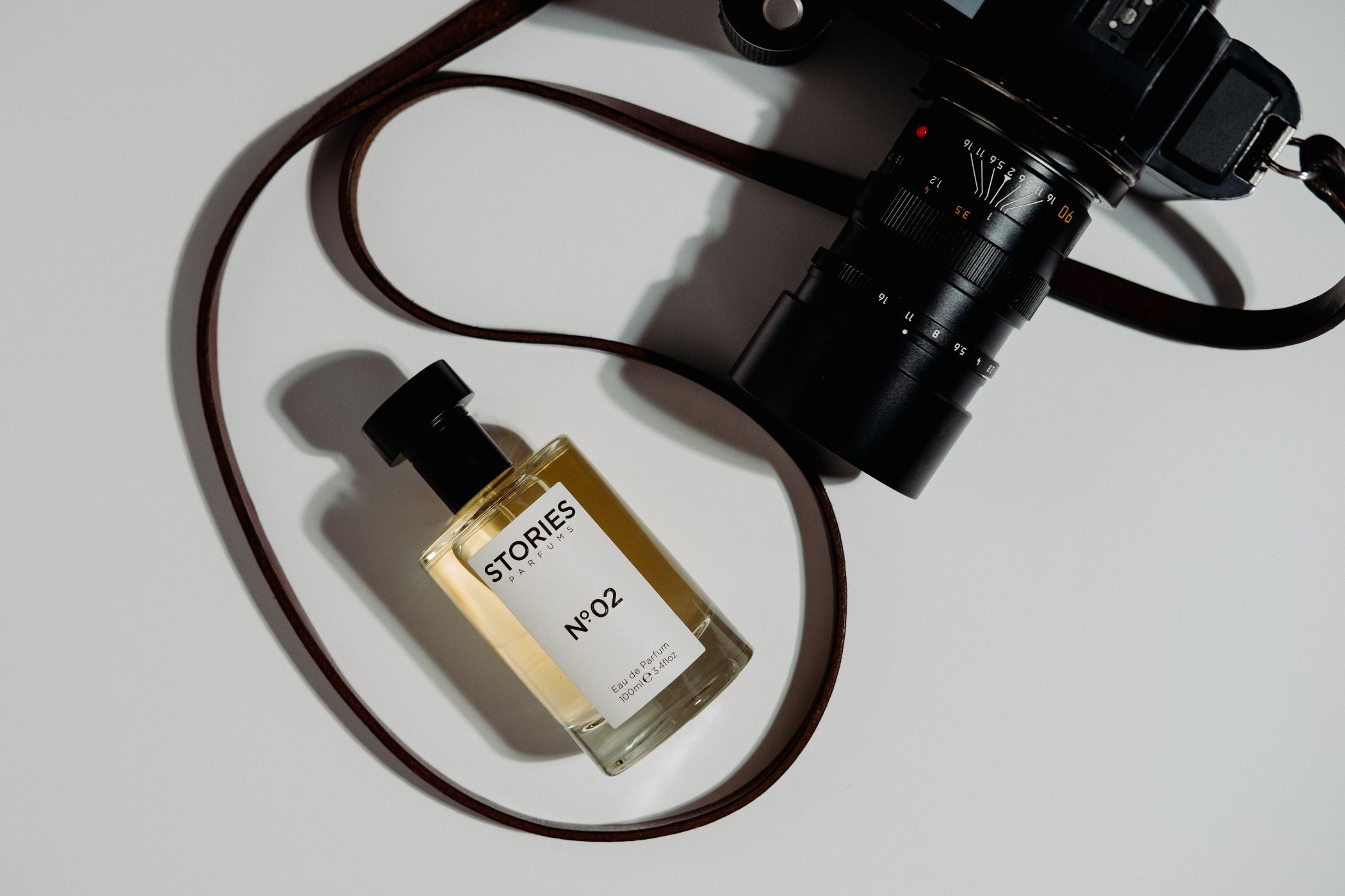 glass bottle of STORIES No.02 perfume next to a camera lense and strap