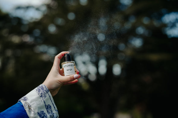 Hand spritzing STORIES Eau de Parfum into the air in a garden