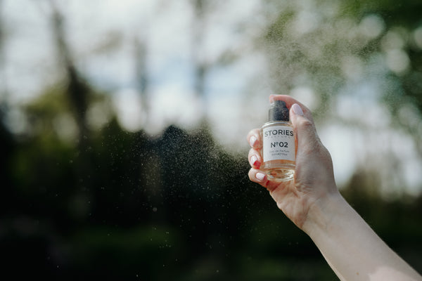 Hand spraying STORIES Eau de Parfum outdoors next to trees