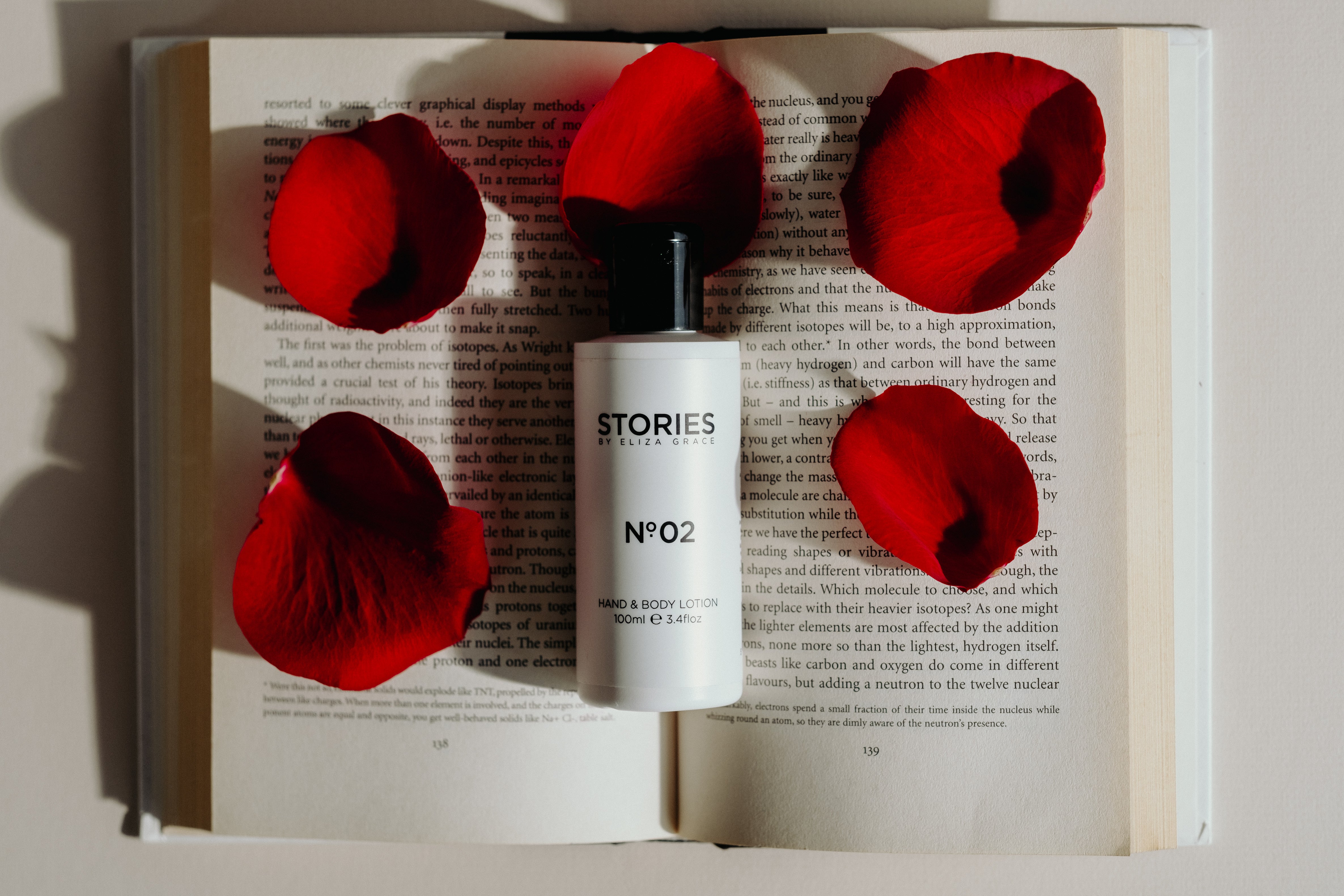 STORIES Parfums Hand and Body Lotion resting on an open book surrounded by red rose petals