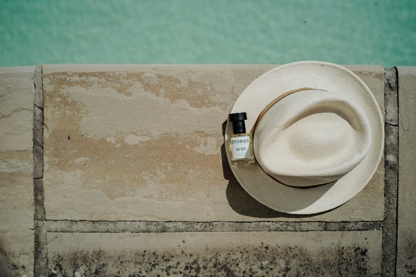 Bottle of STORIES perfume resting on a white straw hat next to a pool