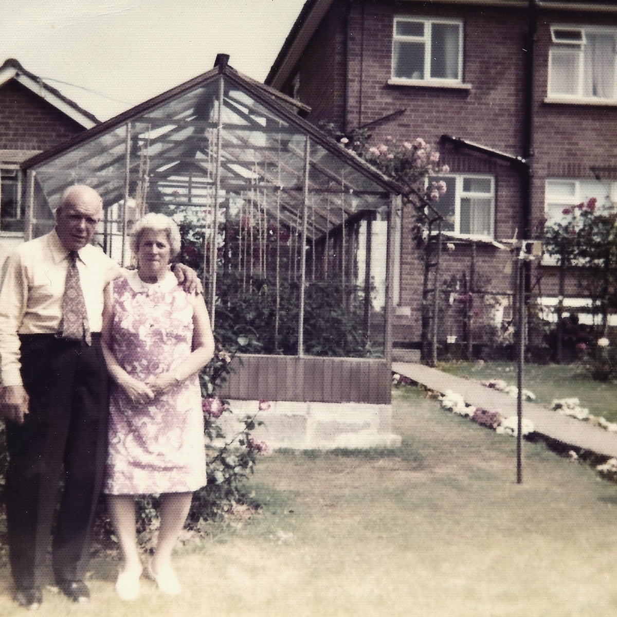 Tonya's grandparents in their garden beside her grandfather's greenhouse, with climbing roses behind