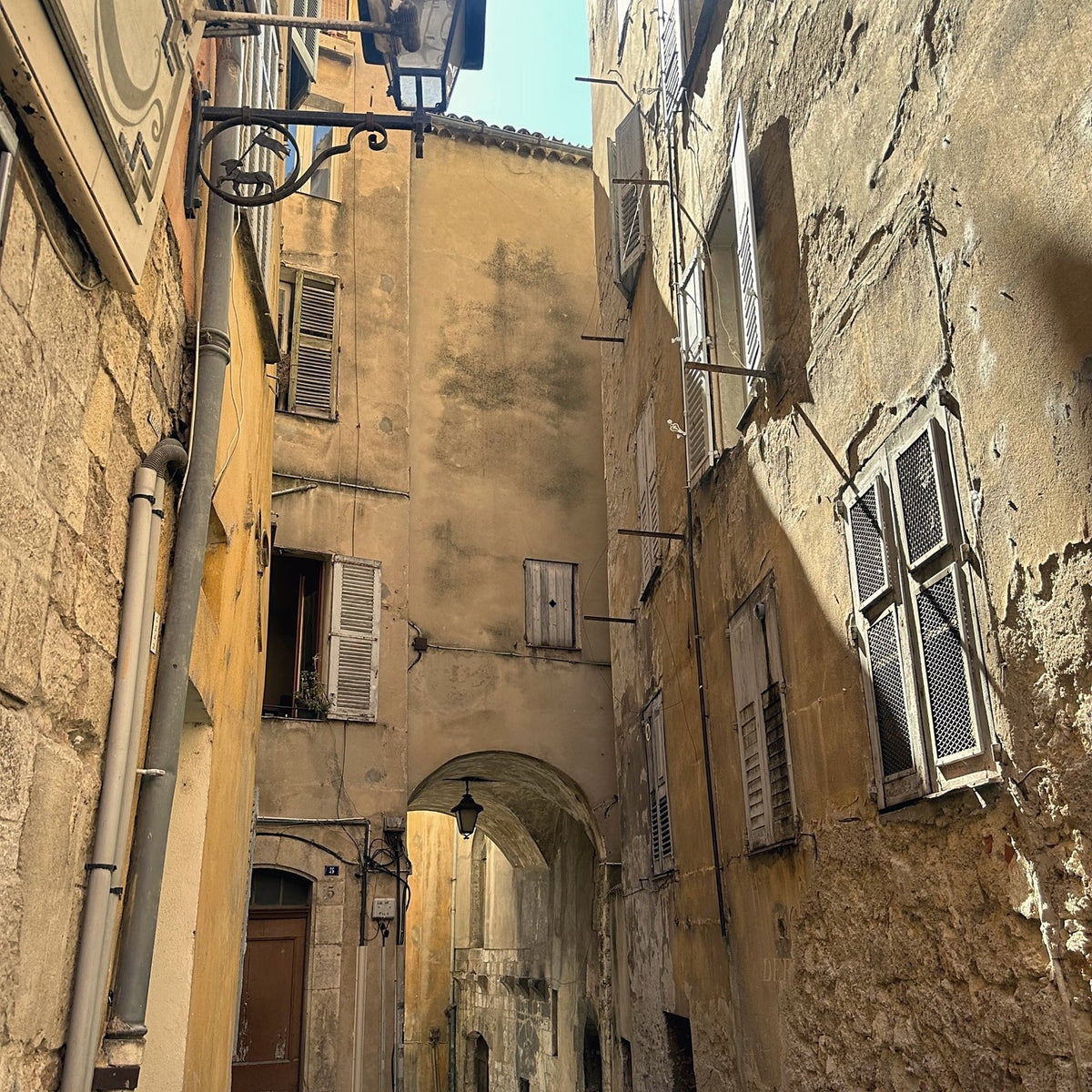 A narrow stone street in the old town of Grasse, with shuttered windows and an archway